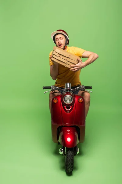 Livreur inquiet en uniforme jaune sur scooter avec boîtes à pizza sur vert — Photo de stock