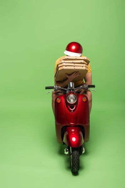 Livreur en uniforme jaune sur scooter visage obscurcissant avec boîtes à pizza sur vert — Photo de stock