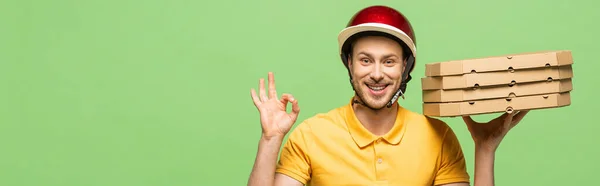 Усміхнений чоловік доставки в жовтій формі доставки піци і показуючи знак ОК ізольовані на зеленому, панорамний постріл — Stock Photo