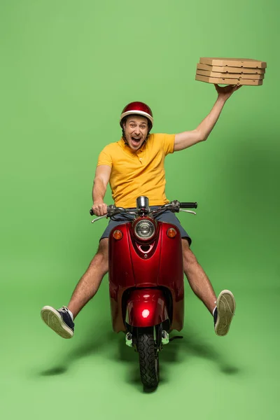 Loco repartidor en uniforme amarillo en scooter entrega pizza en verde — Stock Photo