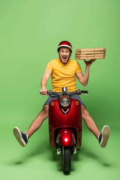 Crazy delivery man in yellow uniform on scooter delivering pizza on green — Stock Photo