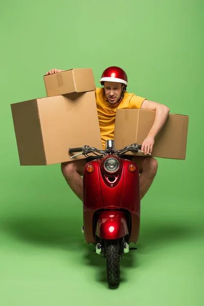 Hombre de entrega cansado en uniforme amarillo en scooter con cajas en verde - foto de stock