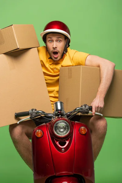 Scared delivery man in yellow uniform on scooter with boxes isolated on green — Stock Photo