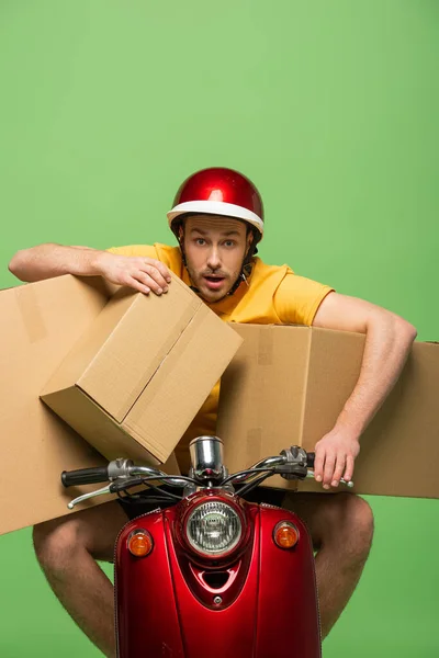 Mad delivery man in yellow uniform on scooter with boxes isolated on green — Stock Photo