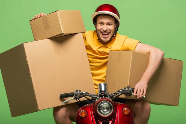 Homem de entrega feliz em uniforme amarelo em scooter com caixas isoladas em verde — Fotografia de Stock