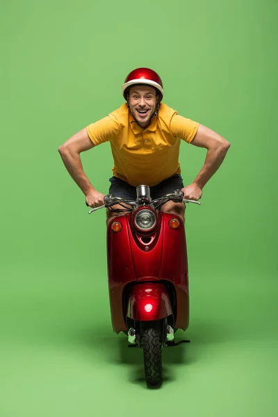 Happy delivery man in yellow uniform and helmet on scooter on green — Stock Photo