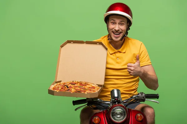 Fattorino sorridente in uniforme gialla su scooter con pizza che mostra pollice in su isolato sul verde — Foto stock