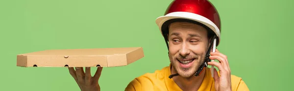 Livreur souriant en uniforme jaune avec pizza parlant sur smartphone isolé sur vert, plan panoramique — Photo de stock