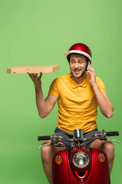 Lächelnder Zusteller in gelber Uniform auf Roller mit Pizza im Gespräch auf Smartphone isoliert auf Grün — Stockfoto