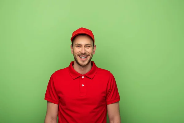 Homem de entrega feliz em uniforme vermelho isolado no verde — Fotografia de Stock