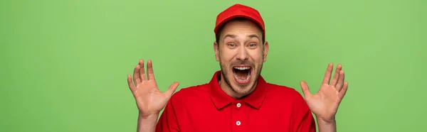 Eccitato uomo di consegna in uniforme rossa mostrando le mani isolate sul verde, colpo panoramico — Foto stock