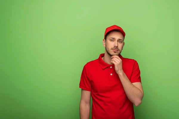 Uomo di consegna pensoso in uniforme rossa su verde — Foto stock