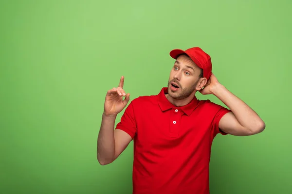 Eccitato uomo di consegna in uniforme rossa mostrando idea gesto sul verde — Foto stock