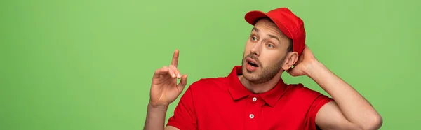 Excité livreur en uniforme rouge montrant geste idée isolé sur vert, panoramique coup — Photo de stock