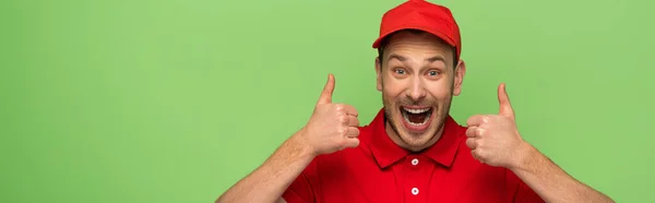 Homem de entrega animado em uniforme vermelho mostrando polegares isolados em verde, tiro panorâmico — Fotografia de Stock