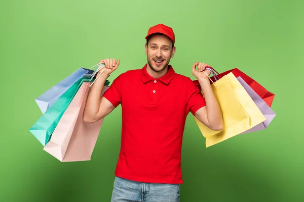 Щасливий чоловік доставки в червоній формі тримає сумки на зеленому — стокове фото