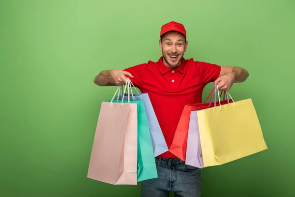 Happy delivery man in red uniform holding shopping bags on green — Stock Photo
