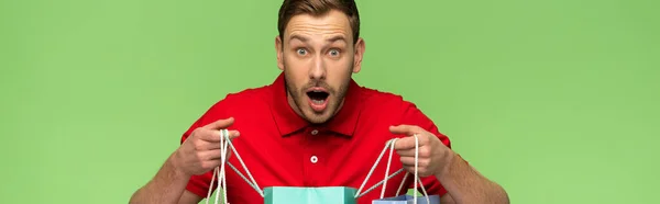 Shocked young man holding shopping bags isolated on green, panoramic shot — Stock Photo