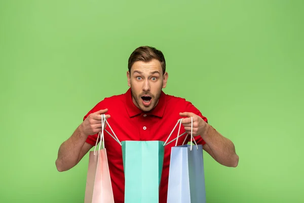 Schockierter junger Mann hält Einkaufstüten isoliert auf Grün — Stockfoto
