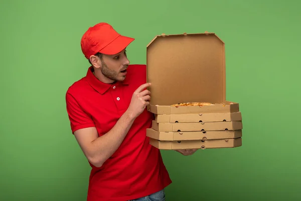 Shocked delivery man in red uniform holding pizza boxes on green — Stock Photo