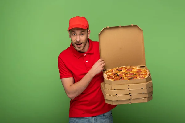 Homem de entrega animado em uniforme vermelho segurando caixas de pizza no verde — Fotografia de Stock