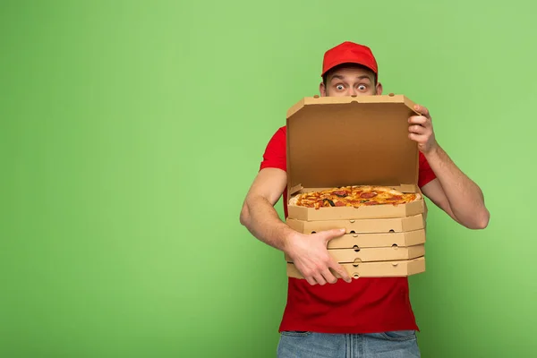 Shocked delivery man in red uniform hiding behind pizza boxes on green — Stock Photo