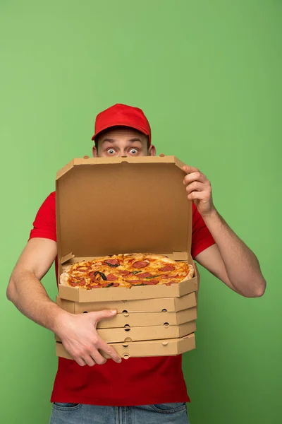 Homme de livraison choqué en uniforme rouge caché derrière des boîtes à pizza sur vert — Photo de stock