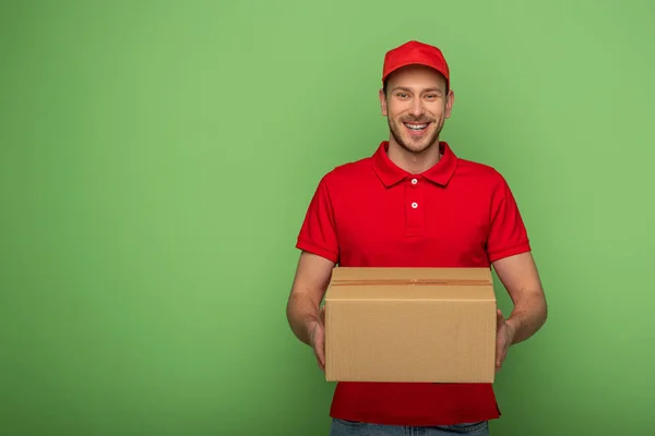 Repartidor sonriente en uniforme rojo que sostiene el paquete en verde - foto de stock