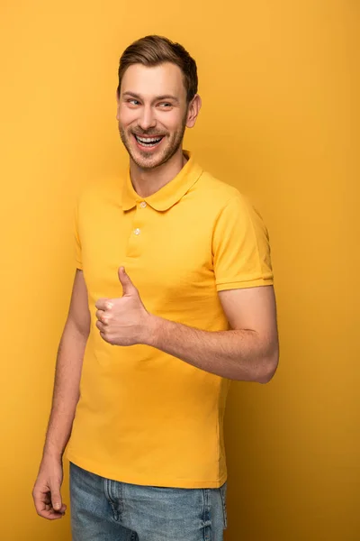 Счастливый красавец в желтом наряде, показывающий большой палец вверх на желтом фоне — стоковое фото
