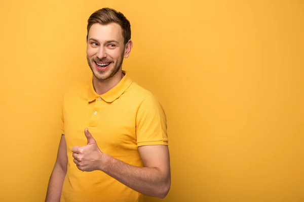 Hombre guapo feliz en traje amarillo que muestra el pulgar hacia arriba en el fondo amarillo - foto de stock