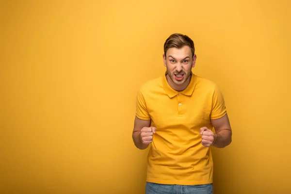 Homme en colère en tenue jaune montrant les poings sur fond jaune — Photo de stock