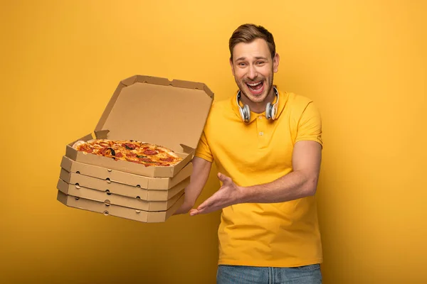 Happy man with headphones in yellow outfit holding pizza on yellow background — Stock Photo