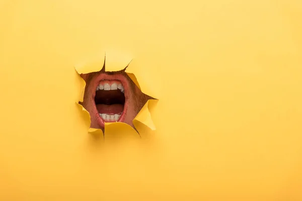 Vista recortada de la boca abierta en agujero de papel amarillo - foto de stock