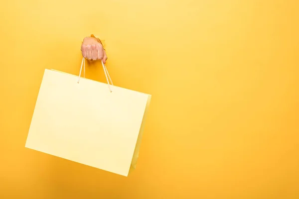 Vista ritagliata dell'uomo che tiene la borsa della spesa nel buco di carta giallo — Foto stock