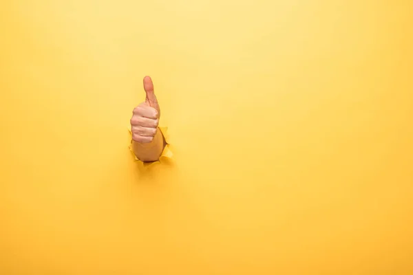 Vista cortada do homem mostrando polegar através de buraco de papel amarelo — Fotografia de Stock