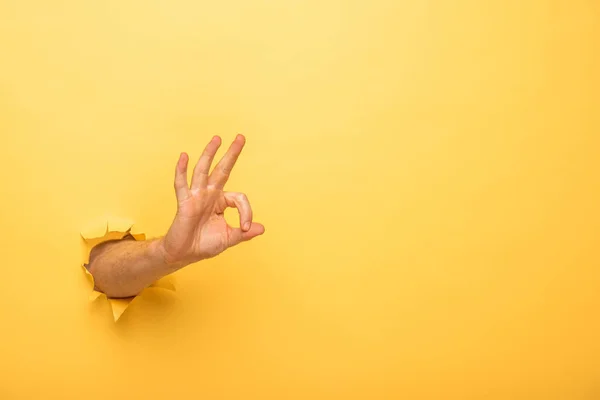 Vue recadrée de l'homme montrant ok signe à travers le trou de papier jaune — Photo de stock