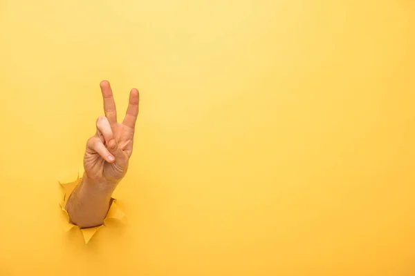 Vista recortada del hombre mostrando señal de paz a través de agujero de papel amarillo - foto de stock