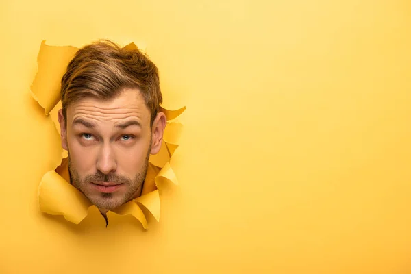 Hombre guapo mirando hacia arriba con la cabeza en agujero de papel amarillo - foto de stock