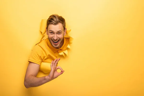 Glücklich schöner Mann in gelbem Outfit in gelbem Papierloch zeigt ok Zeichen — Stockfoto