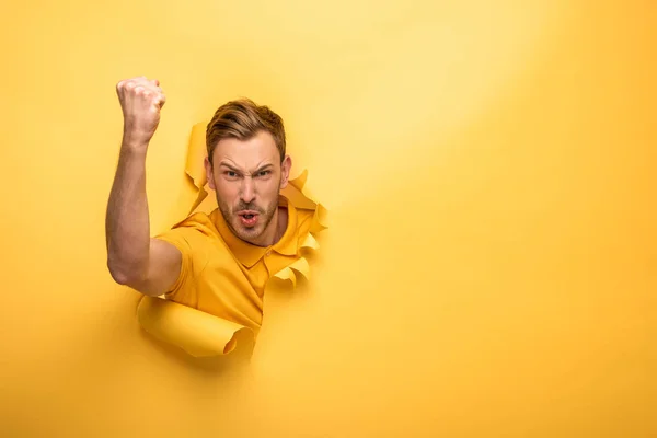Angry handsome man in yellow outfit in yellow paper hole showing fist — Stock Photo