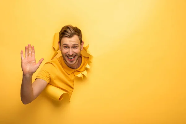 Щасливий красивий чоловік в жовтому вбранні в жовтому паперовому отворі дає високі п'ять — стокове фото