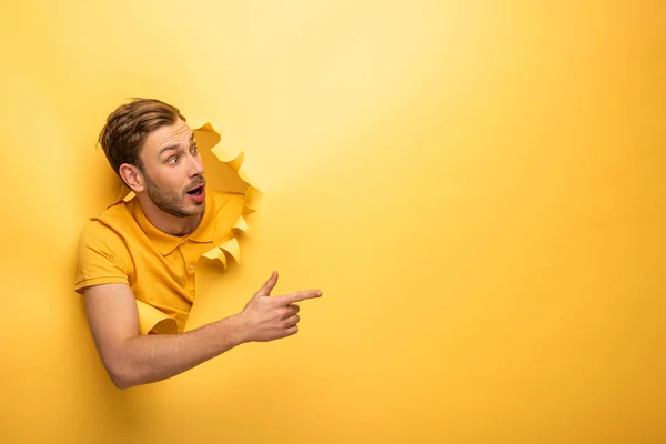 Loco hombre guapo en traje amarillo en agujero de papel amarillo señalando con el dedo a un lado - foto de stock