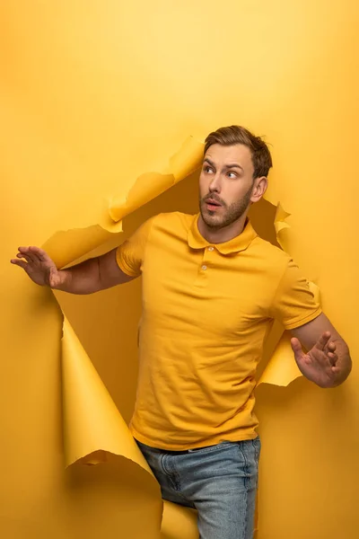 Homem bonito surpreso na roupa amarela andando através do buraco de papel amarelo — Fotografia de Stock