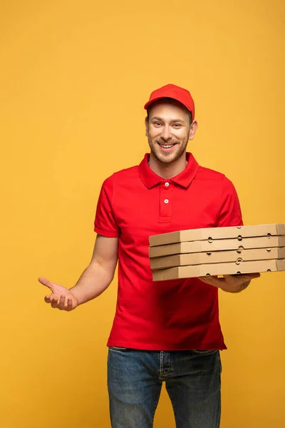 Hombre de entrega feliz en uniforme rojo sosteniendo cajas de pizza aisladas en amarillo - foto de stock