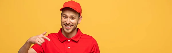 Homem de entrega feliz em uniforme vermelho apontando com o dedo isolado em amarelo, tiro panorâmico — Fotografia de Stock