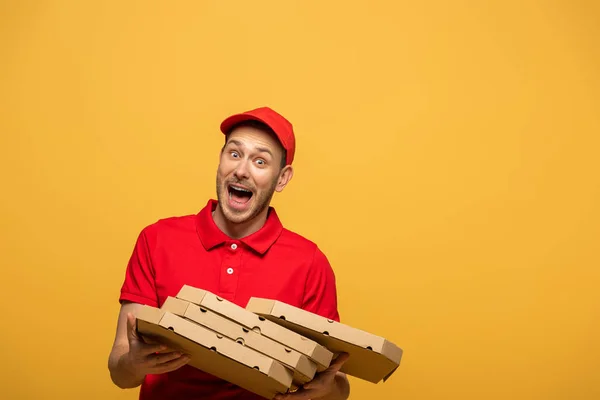 Homem de entrega assustado em uniforme vermelho deixando cair caixas de pizza e gritando isolado no amarelo — Fotografia de Stock