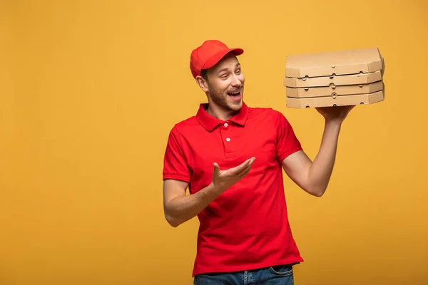 Homem de entrega feliz em uniforme vermelho apontando com a mão para caixas de pizza isoladas em amarelo — Fotografia de Stock