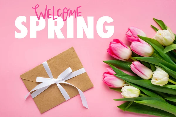 Top view of envelope with bow and bouquet of tulips on pink surface, welcome spring illustration — Stock Photo