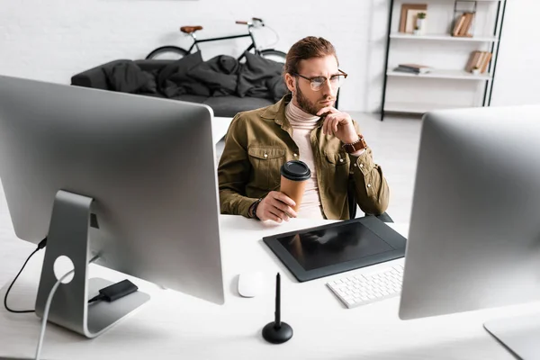 Bel artiste 3d tenant café et regardant moniteur d'ordinateur sur la table dans le bureau — Photo de stock