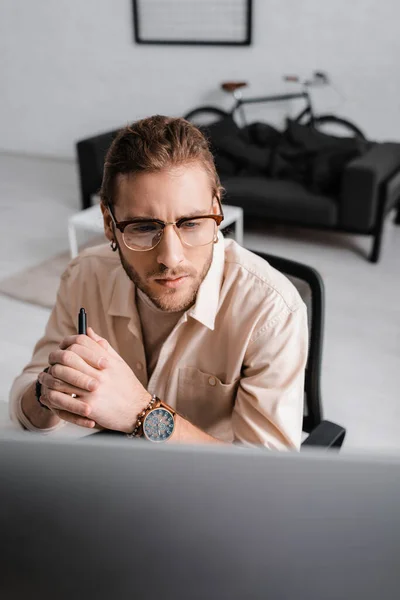 Selektiver Fokus eines gut aussehenden 3D-Künstlers, der den Stift eines Grafiktablets in der Hand hält und im Büro auf den Computermonitor blickt — Stockfoto